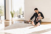 Padre con bambino utilizzando computer portatile seduto sul pavimento — Foto stock
