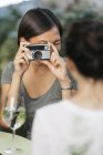 Mujer joven tomando la foto de un amigo con cámara en el café de la acera - foto de stock
