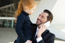 Homme d'affaires souriant au téléphone tenant sa fille — Photo de stock