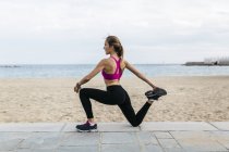 Young woman stretching and warming up for training at beach — Stock Photo