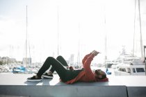 Испания, Барселона. Портрет молодого черного парня в повседневной одежде, лежащего в передвижном положении, с лодками на заднем плане . — стоковое фото