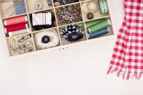 Sewing kit on white fabric with checkered red and white scarf — Stock Photo