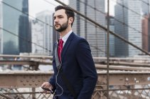 Estados Unidos, Nueva York, Brooklyn bridge, Retrato de un joven hombre de negocios con auriculares y smartphone - foto de stock