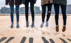 Ноги четырех молодых женщин, прыгающих по песчаному пляжу — стоковое фото
