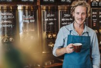 Retrato de tostador de café sonriente sosteniendo la taza de café en la tienda - foto de stock
