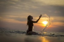 Surfista feminina espirrando água no oceano ao pôr do sol — Fotografia de Stock