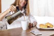 Mulher derramando café em xícara na mesa de café da manhã — Fotografia de Stock