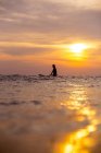 Surfista femminile nell'oceano al tramonto con cielo romantico — Foto stock
