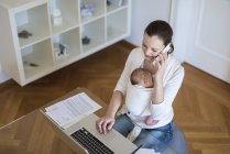 Erhöhter Blick auf freiberufliche Mutter mit Säugling im Tragetuch bei der Arbeit im Home Office — Stockfoto