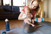 Mãe com bebê exercitando com haltere em casa — Fotografia de Stock