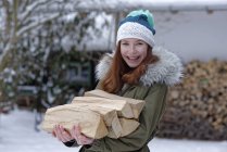 Portrait d'adolescente souriante portant du bois de chauffage en hiver — Photo de stock