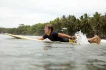 Indonésia, Java, homem deitado na prancha de surf no mar — Fotografia de Stock