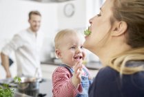Mother with baby girl in kitchen eating herbs — Stock Photo