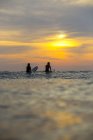 Indonesien, Bali, zwei Surferinnen im Ozean bei Sonnenuntergang — Stockfoto