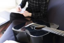 Mann schreibt Noten, Gitarre im Vordergrund — Stockfoto