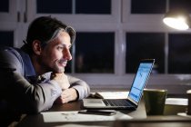 Sorrindo homem trabalhando até tarde no escritório com laptop — Fotografia de Stock
