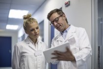 Man and woman in lab coats looking at tablet together in clinic — Stock Photo