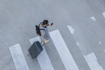 Бізнесмен з багажем, що перетинає вулицю під час використання мобільного телефону — стокове фото