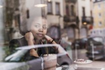 Молода жінка, сидячи в кафе за шибці і дивиться з вікна — стокове фото