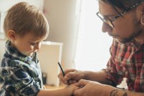 Father painting tattoo on sons hand — Stock Photo