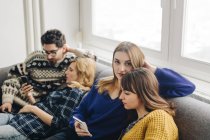 Quatre amis avec des smartphones sur le canapé dans le salon — Photo de stock