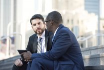 Dois empresários sentados nas escadas conversando e compartilhando tablet — Fotografia de Stock