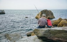 Abuelo y nieto pescando juntos en la roca en el mar - foto de stock