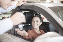 Concessionnaire de voiture donnant la clé à une femme assise dans la voiture — Photo de stock