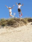 Junge und Mädchen springen von Stranddüne — Stockfoto