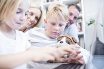 Brother and sister with cuddly toy using laptop together with parents on background — Stock Photo