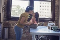 Мать целуется с дочерью, сидящей на кухонном столе — стоковое фото