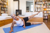 Mulher se exercitando no tapete de ginásio na sala de estar — Fotografia de Stock
