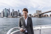 Businesswoman standing on boat and using cell phone, Brooklyn, USA — Stock Photo