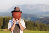 Austria, Mondsee, Mondseeberg, young man covering his face with a basketball — Stock Photo