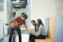 Jovem em bicicleta conversando com colegas usando laptop — Fotografia de Stock