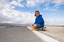 Espagne, Tenerife, garçon souriant assis sur une planche à roulettes au bord de la route — Photo de stock