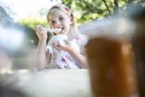 Girl eating at garden table and looking at camera — Stock Photo
