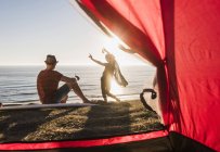 Junges Paar campiert am Meer, beobachtet den Sonnenuntergang am Zelt, Mädchen tanzen am Strand — Stockfoto