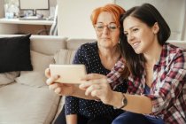 Madre e figlia adulta scattare selfie su smart phone seduto sul divano — Foto stock