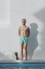 Jeune homme debout au bord de la piscine à côté de l'ananas — Photo de stock
