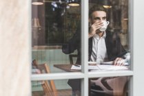 Young businessman drinking coffee in a cafe behind windowpane — Stock Photo