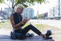 Улыбающаяся молодая африканка с сотовым телефоном и наушниками — стоковое фото