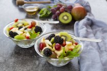 Salada de frutas com amoras em tigelas na superfície cinza — Fotografia de Stock