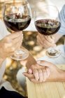Close-up of senior couple hands with glasses of red wine and holding hands outdoors — Stock Photo