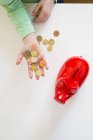 Mädchenhand mit Münzen und einem roten Sparschwein — Stockfoto