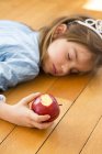 Menina deitada no chão de madeira e segurando maçã vermelha mordida — Fotografia de Stock