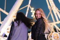 Deux jeunes femmes heureuses debout sur une fête foraine la nuit — Photo de stock