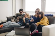 Quatre amis avec des smartphones sur le canapé dans le salon — Photo de stock