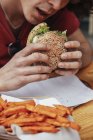 Young man eating vegan hamburger and sweet potato fries — Stock Photo