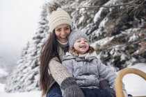 Happy mother with daughter on sledge in winter landscape — Stock Photo